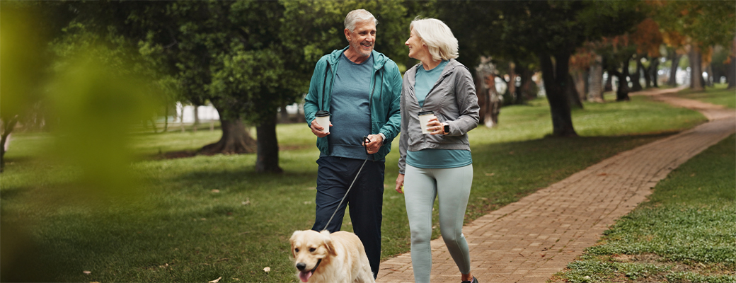 Image of senior couple walking their dog down a park path